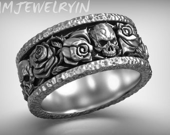 Könnte beinhalten: Ein silberner Ring mit einem Totenkopf- und Rosenmotiv. Der Ring ist texturiert und hat ein breites Band.