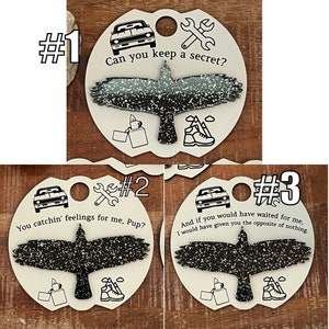 May include: Three round white keychains with black and white images of a bird, a car, and a wrench. Each keychain has a different saying: "Can you keep a secret?", "You catchin' feelings for me, Pup?", and "And if you would have waited for me, I would have given you the opposite of nothing."