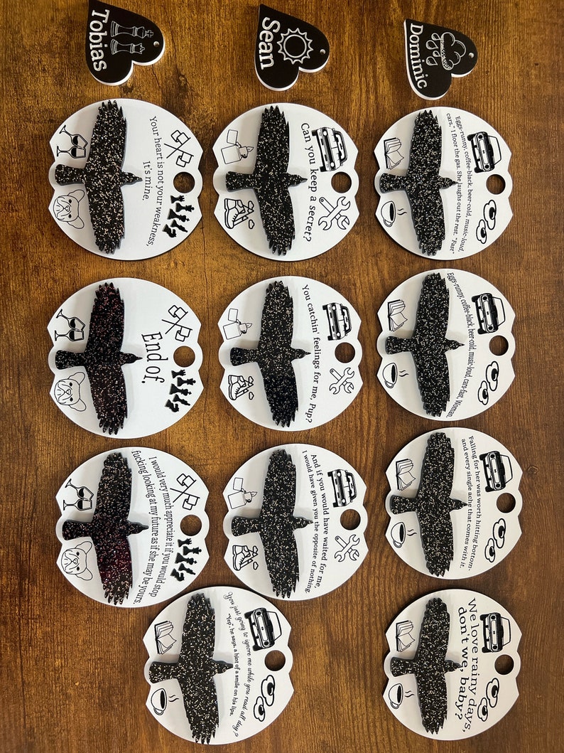 May include: Nine round white and black paper ornaments with a black crow design and text. The text includes quotes such as "Your heart is not your weakness, it's mine." and "Can you keep a secret?"