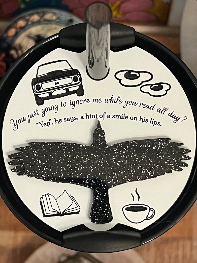 May include: A white tumbler lid with a black silhouette of a bird, a book, a cup of coffee, and two fried eggs. The text "You just going to ignore me while you read all day? "Yep", he says, a hint of a smile on his lips." is printed on the lid.