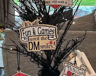 May include: A black twig tree with five wooden ornaments. The ornaments are decorated with dice and text. The text on the ornaments reads "It's all Fun & Games until the DM smiles!" "Just roll with it" "The Dice Giveth & The Dice Taketh Away" "Ok how bad could it be?" and "20".