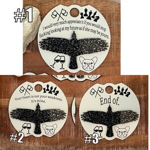 May include: Three white circular ornaments with black glitter accents. Each ornament features a black silhouette of a bird with a French bulldog, a pair of wine glasses, and a set of chess pieces. The text on the ornaments reads: "I would very much appreciate it if you would stop fucking looking at my future as if she may be yours.", "Your heart is not your weakness. It's mine.", and "End of."