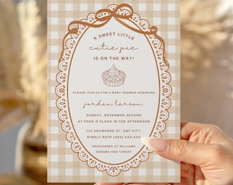 May include: Baby shower invitation with a tan and white gingham background. The invitation has a brown oval frame with the text "A sweet little cutie pie is on the way!" and details for the event, including the name Jordan Larson.