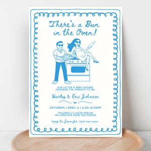 Può includere: Invito per baby shower con illustrazioni e testo blu. La frase "There's a Bun in the Oven!" è in alto. L'invito include i nomi Harley & Eric Johnson, la data, l'ora e i dettagli del luogo, il tutto all'interno di un bordo blu.