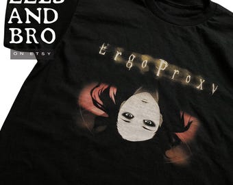 May include: Black t-shirt featuring the text "Ergo Proxy" above a stylized illustration of a face with dark hair and pale skin. The shirt also has the text "EELS AND BRO" and the Etsy shop URL.