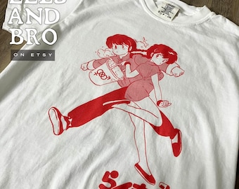 May include: White t-shirt featuring a red graphic of two anime characters in motion. The design includes Japanese text and the words "FLUID SINCE 1986". The shirt also has the text "EELS AND BRO" and "ON ETSY".
