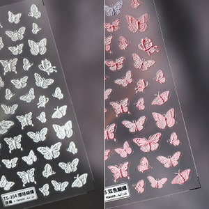 Könnte beinhalten: Zwei Bögen Schmetterlings-Nagelkunst-Aufkleber. Ein Bogen zeigt weiße Schmetterlinge, der andere rote Schmetterlinge. Die Schmetterlinge sind unterschiedlich groß und auf einem transparenten Hintergrund geprägt. Der Text "TS-254" und "TS-255" ist sichtbar.