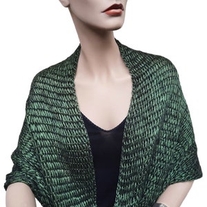 May include: A green knitted shawl with a subtle shimmer. The shawl is draped over a mannequin's shoulders and has a V-neck opening.