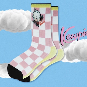 May include: A pair of pink and white checkered socks with a yellow trim. The socks feature a cartoon image of a Kewpie doll with a flower and the word "Kewpie" on the front.