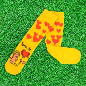 May include: Yellow socks with a red heart pattern and the text "Love is..." with a cartoon illustration of a girl holding a red heart balloon.