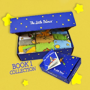 May include: A blue box with stars and the text "The Little Prince" on the lid. The box is open and contains a set of socks with different designs featuring characters and elements from the book "The Little Prince". The box also includes a small book with the title "The Little Prince" on the cover. The text "Book 1 Collection" is printed on the front of the box.