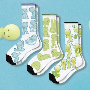 May include: Four pairs of white socks with colorful cartoon characters printed on them. The socks feature a variety of characters, including a person with a crown, a person with a star, and a person with a heart. The socks are all different colors, including blue, green, yellow, and red.