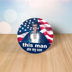 Op de afbeelding: Een ronde button met een afbeelding van een man voor een Amerikaanse vlag. De tekst "this man ate my son" is in het wit gedrukt op een blauwe banner aan de onderkant van de button.