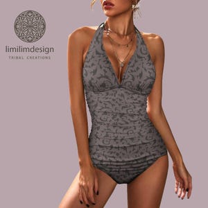 May include: Grey halter-neck swimsuit with a dark grey pattern. The one-piece swimsuit has a plunging neckline and matching bottoms. The swimsuit is from "limilimdesign TRIBAL CREATIONS".