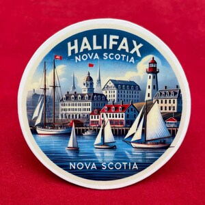 May include: A round, white coaster with a detailed illustration of Halifax, Nova Scotia. The image features sailboats, a lighthouse, and buildings along the waterfront. The words "HALIFAX" and "NOVA SCOTIA" are prominently displayed in blue text.