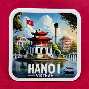 May include: Square magnet with a scenic illustration of Hanoi, Vietnam. The image depicts a red-roofed pagoda on a lake, with a bridge, buildings, and a tower in the background. The text "HANOI VIETNAM" is clearly visible.