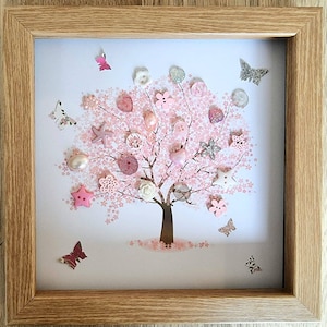 May include: A framed picture with a tree design made from pink and white buttons and embellishments. The tree has a brown trunk and branches, with pink blossoms. Several butterfly cutouts are scattered around the tree, all within a light wood frame.