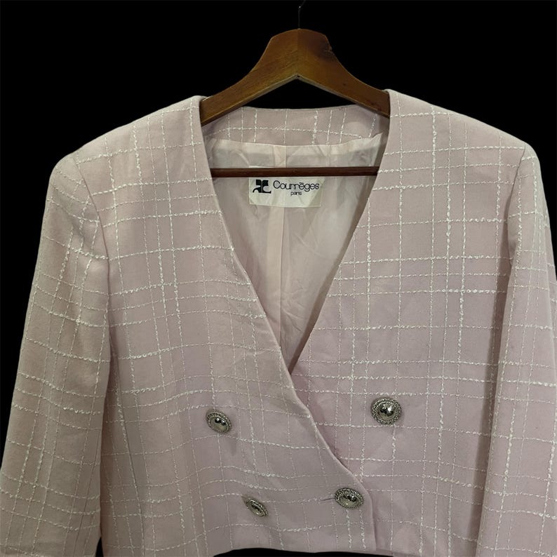 May include: A pink blazer with a white grid pattern and silver buttons. The blazer has a v-neck and a double-breasted closure. The label reads "Courr&egrave;ges Paris".