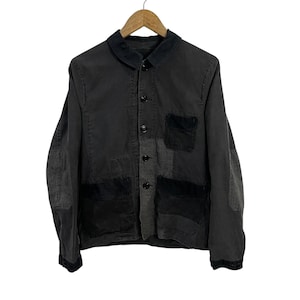 May include: A charcoal gray button-up jacket featuring a dark collar, long sleeves with elbow patches, and multiple pockets. The garment includes a chest pocket and two lower front pockets, all constructed with contrasting dark fabric panels.