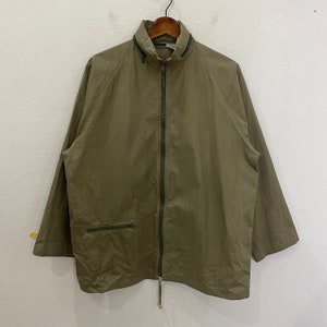 May include: A green zip-up jacket with a drawstring at the bottom. The jacket has a zippered pocket on the left side.