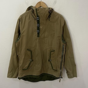 May include: A tan anorak jacket with a hood, three buttons, and two front pockets. The jacket has a green lining and trim, and a zipper on the side. The jacket is hanging on a wooden hanger.