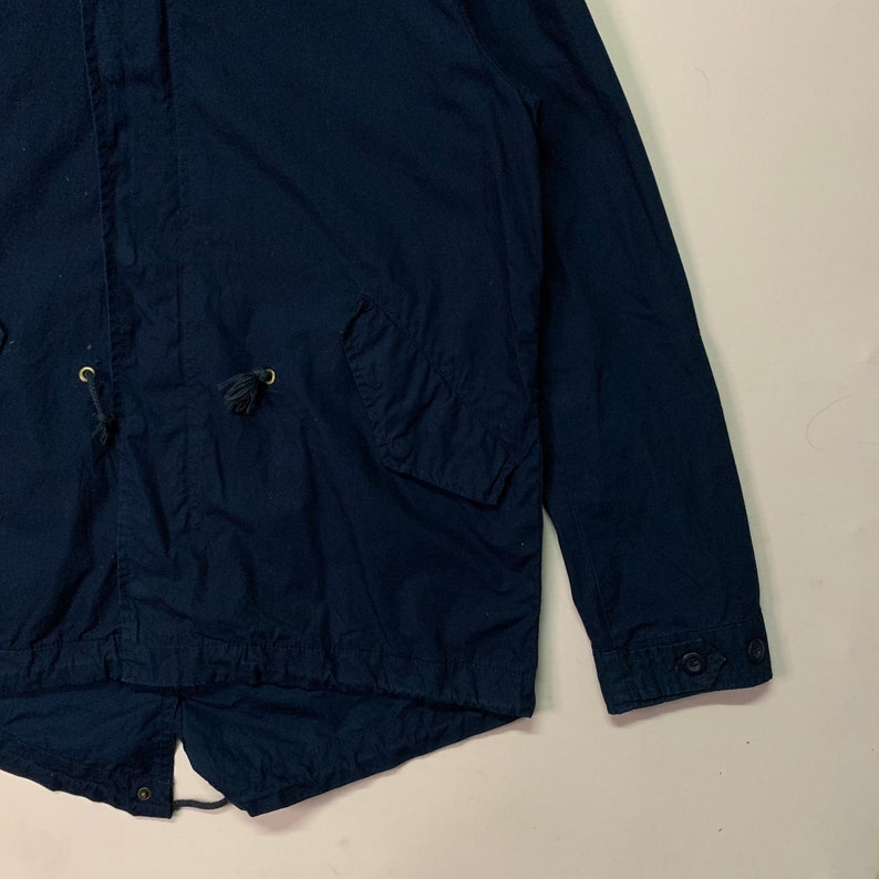 May include: Navy blue jacket with a drawstring hood and two front pockets. The jacket has buttoned cuffs and a drawstring waist. The fabric appears to be a lightweight cotton or cotton blend.