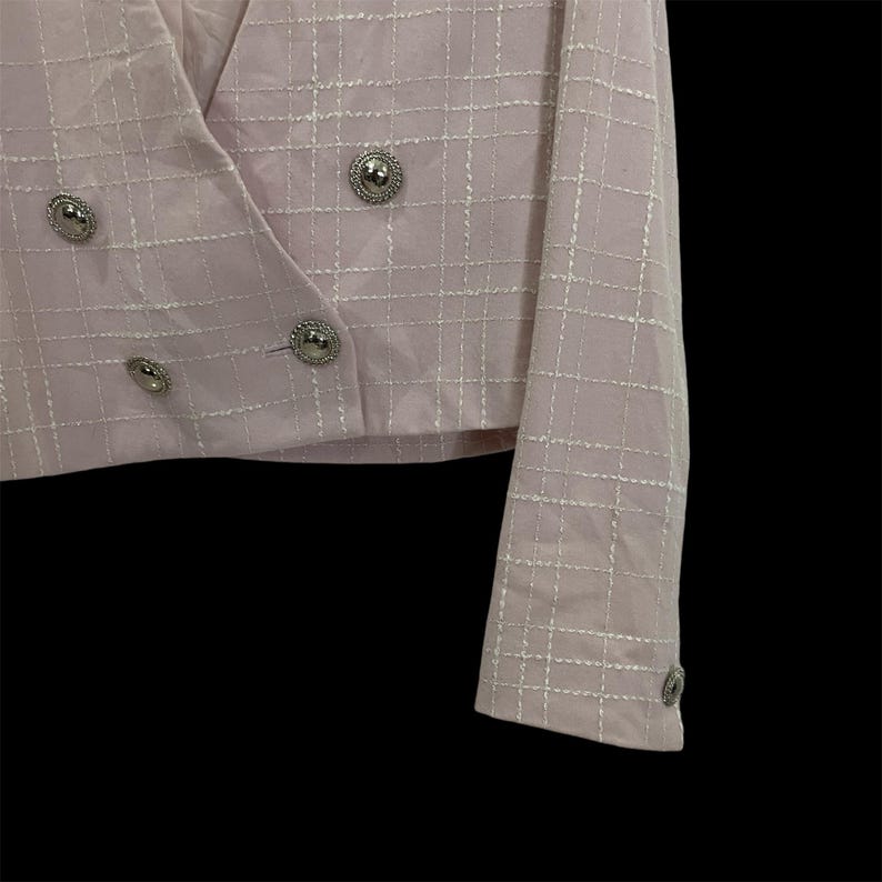 May include: A pink blazer with a white grid pattern and silver buttons. The blazer has a double-breasted closure and long sleeves.