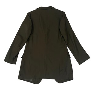 Puede incluir: Una americana de color verde oliva oscuro con cuello estructurado, mangas largas y dos bolsillos con solapa situados en los laterales inferiores. La prenda se muestra desde la parte posterior, destacando un dise&ntilde;o liso con costuras verticales.