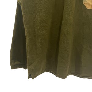 May include: Olive green fleece pullover with long sleeves. The garment has a soft, textured appearance and a relaxed fit. The image shows a portion of the top, highlighting the fabric's details and the overall style.