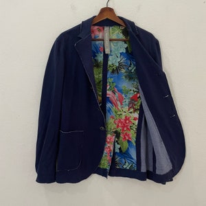 May include: A navy blue blazer with a floral print lining. The lining features a tropical design with pink, green, and blue flowers. The blazer has a single button closure and a pocket on the left side.