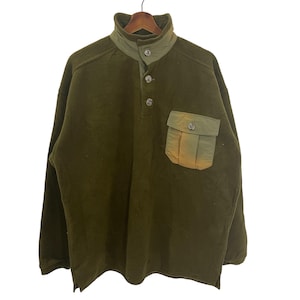 May include: Olive green fleece pullover with a high collar and a button-down placket. Features a contrasting green pocket on the chest. The garment is hanging on a wooden hanger against a white background. The fleece material appears soft and warm.