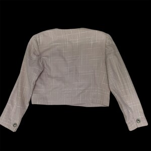 May include: A light pink cropped blazer with a white checkered pattern. The blazer has long sleeves and a button closure.