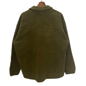 May include: Olive green fleece jacket with a collared neckline and button closure. The jacket is hanging on a wooden hanger. The back of the jacket is visible, showing the seams and the texture of the fleece material.