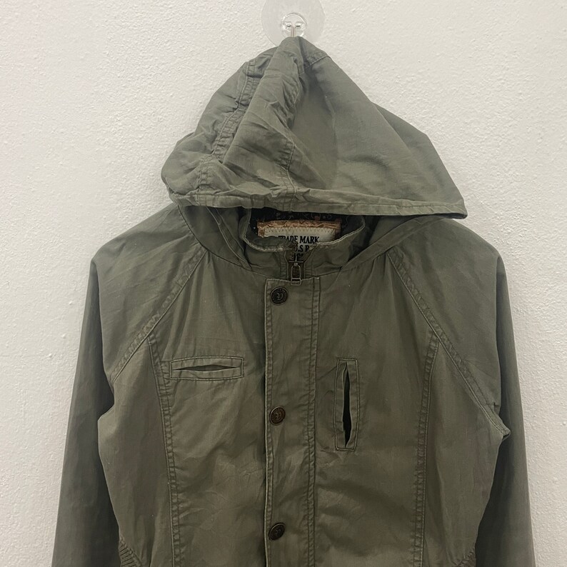 May include: A green hooded jacket with a button closure and a zipper. The jacket has a pocket on the left chest and a small pocket on the right side. The label on the jacket reads "Trade Mark Is R".