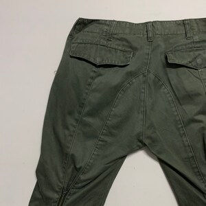 May include: A pair of dark green cargo pants with a zipper at the bottom of each leg. The pants have two back pockets and a button fly.