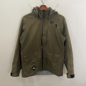 Może przedstawiać: Zielona kurtka z kapturem, czarnym zamkiem błyskawicznym i czarnymi lamówkami. Kurtka ma logo na lewej piersi z napisem "TACHI" i drugie logo na lewym rękawie.