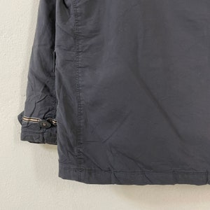 Pode incluir: Casaco cinza escuro com punho abotoado e costura na frente. O punho tem um detalhe de listras marrons e bege. O casaco &eacute; feito de um material liso, possivelmente nylon.