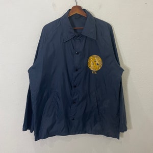 Puede incluir: Una chaqueta de nylon azul marino con un parche bordado en oro que dice "Pittsburgh Theological Seminary 1794 P.T.S."