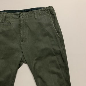 May include: A pair of dark green chino pants with a black waistband and a button fly.