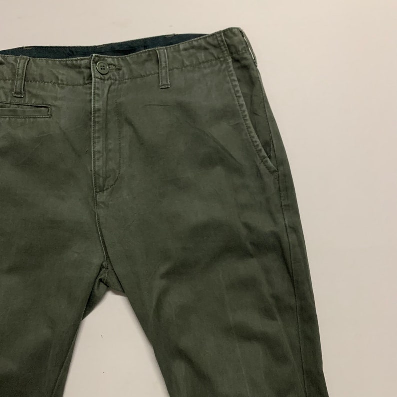 May include: A pair of dark green chino pants with a black waistband and a button fly.