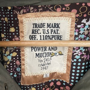 May include: A brown and gold label with white text that reads "TRADE MARK REC. U.S PAT. OFF. 110%PURE POWER AND MOTION Von Dutch established 1947" with a stylized eye and wings logo. The label has a size "L" tag.