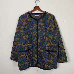 May include: A blue, green, and yellow floral patterned cardigan with a button-up front and two pockets. The cardigan has a black trim around the edges.