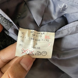 Op de afbeelding: Een wit label met zwarte tekst en symbolen. Het label bevat de volgende informatie: NO. BPI-SR SA GA 073 BQ サイズ C96-W86-T170 COL. 3 INS. 30538. Het label bevat ook symbolen voor chemische reiniging, strijken en handwas.