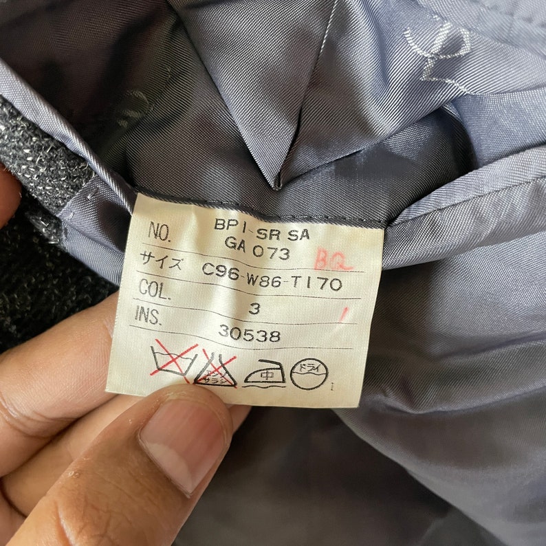 Op de afbeelding: Een wit label met zwarte tekst en symbolen. Het label bevat de volgende informatie: NO. BPI-SR SA GA 073 BQ サイズ C96-W86-T170 COL. 3 INS. 30538. Het label bevat ook symbolen voor chemische reiniging, strijken en handwas.