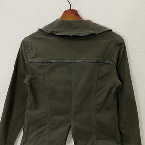 May include: A dark green utility jacket with a collared neckline and a leather trim detail. The jacket has long sleeves and a button closure.