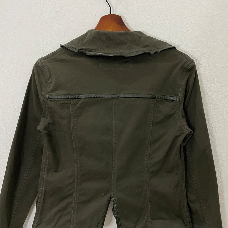 May include: A dark green utility jacket with a collared neckline and a leather trim detail. The jacket has long sleeves and a button closure.