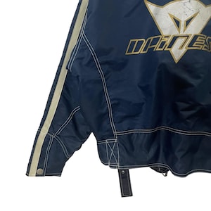 May include: A navy blue jacket with white piping and a DAINESE logo on the back. The jacket has a zipper closure and a white drawstring.