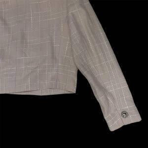 May include: A light pink cropped jacket with a white grid pattern and a silver button on the cuff.