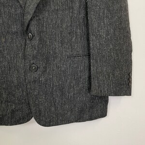 Op de afbeelding: Een donkergrijze blazer van een getextureerde stof. De blazer heeft een enkele knoopsluiting en twee zakken.