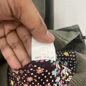 May include: A close-up of a white tag with black text that reads "NO. 6126 2380". The tag is attached to a brown and green garment with a floral pattern.